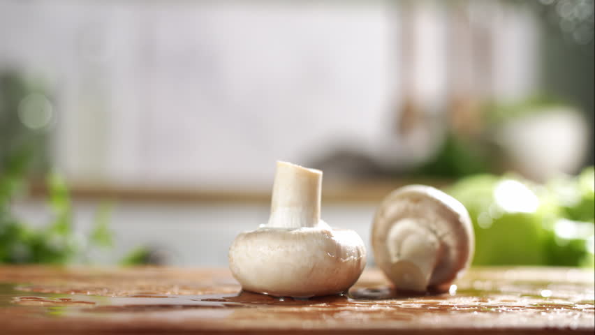 Slow motion of white and brown mushrooms falling on wet wooden board in a kitchen