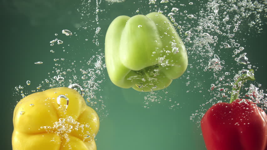 Slow motion of Colorful peppers falling into water on green background