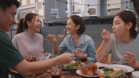 Mom enjoy thai meal cooking for family day meet talk home dining at dine table cozy patio. Group asia people young adult man woman friend fun joy relax warm night time picnic eat yummy food with mum.の動画素材