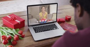 Happy biracial woman opening gift and making valentine's day video call on laptop. valentine's day celebration, romance and communication technology.