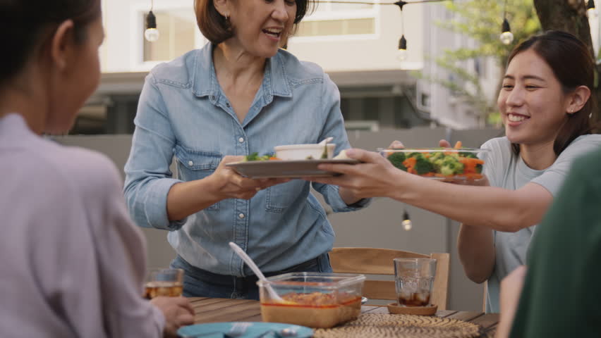 Mom enjoy cooking for family day dining at dine table cozy patio front yard home. Mum passing food serving drink to group four asia people young adult man woman friend fun joy relax warm picnic eating | Shutterstock HD Video #1100815195