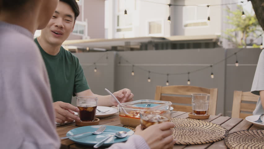 Mom enjoy cooking for family day dining at dine table cozy patio front yard home. Mum passing food serving drink to group four asia people young adult man woman friend fun joy relax warm picnic eating Royalty-Free Stock Footage #1100815197