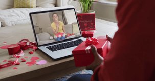 Happy biracial woman opening gift and making valentine's day video call on laptop. valentine's day celebration, romance and communication technology.