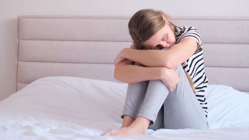 Upset young woman sitting on bed with hidden head. Depression in a woman. Problem, stress