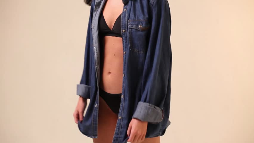 Sexy girl in an unbuttoned denim shirt and black lingerie, posing on a white background, close-up of the body. Young woman in an blue denim shirt and black sexy lingerie on a white background,close up