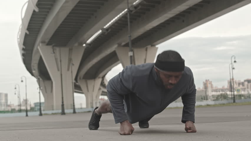 Stab shot of sportive African-American man doing push ups on fists at outdoor workout on cold morning
