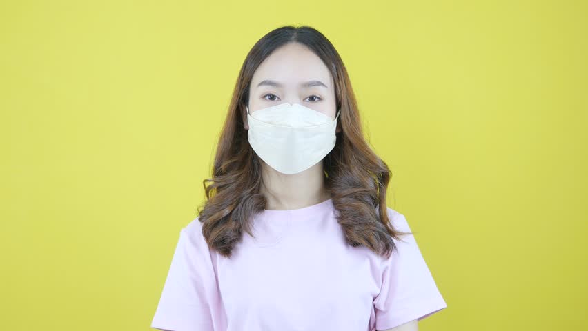 Young Asian woman advised to wear a mask in public on a yellow background. Royalty-Free Stock Footage #1100823215