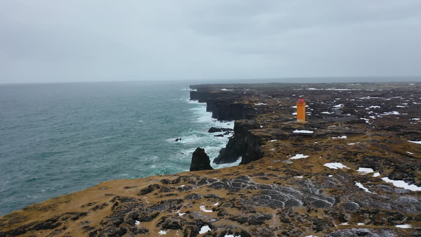 4K aerial footage of an orange lighthouse in northern Iceland on a snowy day in winter.