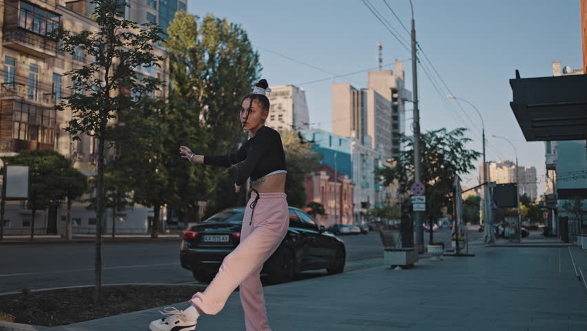 Young woman dances contemporary style on city street and enjoys life being modern dancer. Lady wearing black blouse demonstrates flexible body moves on street Royalty-Free Stock Footage #1100825783