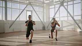 Slow motion. Athletic man and woman lunging forward on two leg in sync, to strengthen muscles of the thighs and buttocks during workout indoors. Training under the guidance of a professional trainer - Powered by Shutterstock - Get 15% off with code: PIKWIZARD15