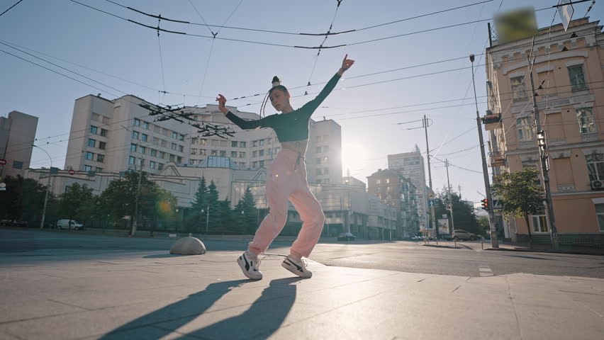 Young woman enjoys dancing on city square. Lady dancer demonstrates first-class performance at back sunrise. Woman expresses feelings through hip-hop dance | Shutterstock HD Video #1100826301