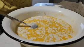 A metal bowl with a mixture of milk, margarine and yeast. Adding flour, making pastry dough, pie, pizza, bread. Video of female hands pouring flour into a bowl.