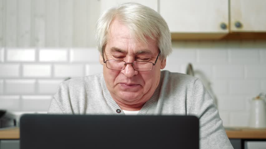 Senior Grey haired 60s - 70s Aged man sitting at table, looking at laptop at home. Older Smile Man working, watching news, content. Old People using modern technology concept, e-learning, education. | Shutterstock HD Video #1100827627