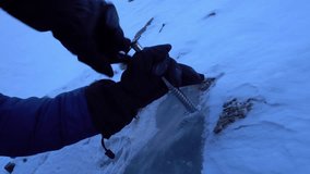 The guy twists a climbing screw into the ice. The ice drill breaks through the ice, which causes it to crack. There are frozen rocks in the glacier, white snow on top. Preparing for the descent - Powered by Shutterstock - Get 15% off with code: PIKWIZARD15