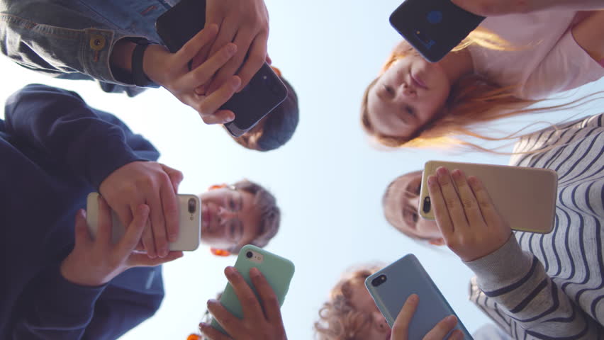 Bottom view of school children use smartphone outdoors. Teenage kids in circle chat on mobile phones. High school students play on cellphones. Children use phone. Realtime  Royalty-Free Stock Footage #1100828617