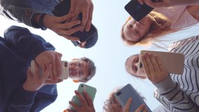 Bottom view of school children use smartphone outdoors. Teenage kids in circle chat on mobile phones. High school students play on cellphones. Children use phone. Realtime  - Powered by Shutterstock - Get 15% off with code: PIKWIZARD15