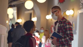 Young male teacher in medical face mask helping African-American student. Teen boy in safety mask talk to teacher in school corridor. High school professor consult student. Realtime - Powered by Shutterstock - Get 15% off with code: PIKWIZARD15