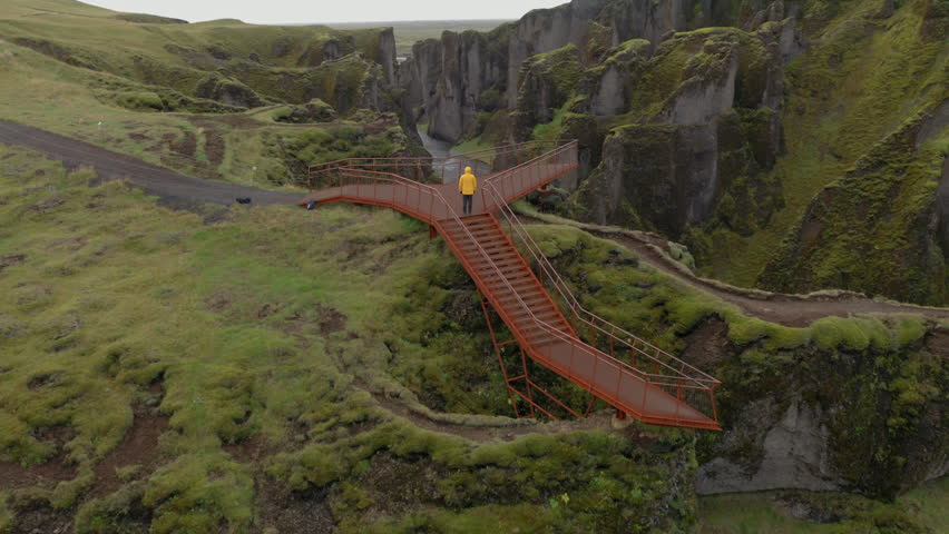 Aerial: One man with yellow jacket walks on the platform towards the Fjadrargljufur Canyon in Iceland