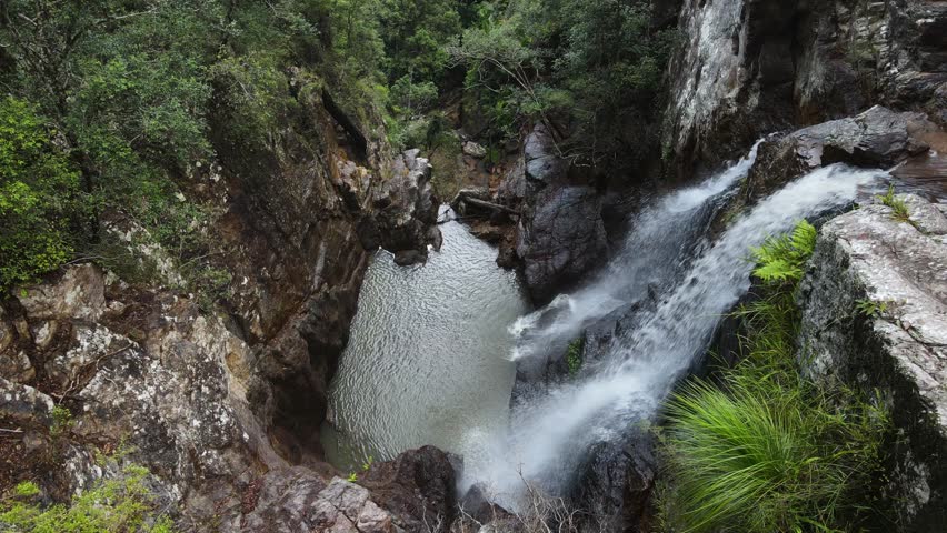 Twin waterfalls cascading down an old-growth rainforest into a natural rock formation swimming hole.