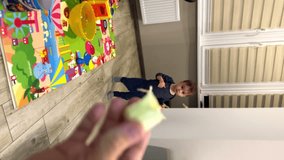 Parent’s hand is holding the a piece of banana. Cute kid comes up and takes a bite. Healthy snack for a child. Vertical video.