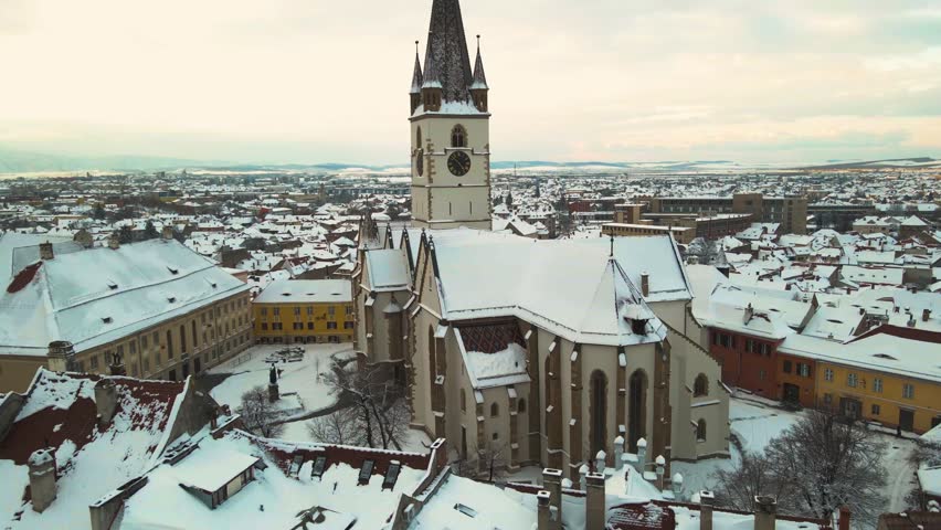 Aerial view of the medieval city center of Sibiu, Romania in winter at sunset. The footage was made from a drone while picking up altitude and with the Evangelic cathedral in the view. 