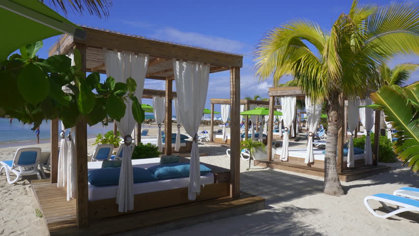 Beach cabanas overlooking the Caribbean Sea. Relax in the shade. Beach, sand, umbrellas, loungers, curtains, palm trees, beach beds. Adrenaline Beach, Labadee, Haiti private resort by Royal Caribbean. Royalty-Free Stock Footage #1100831957