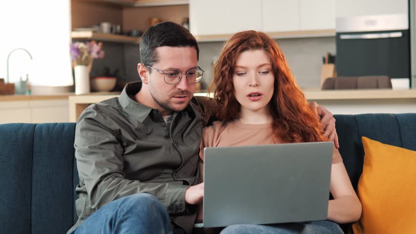 Young amazed family happy couple use laptop read news online received great e-mail scream with joy celebrating unbelievable opportunity hugging each other. Lottery win, auction, betting success. Royalty-Free Stock Footage #1100834801