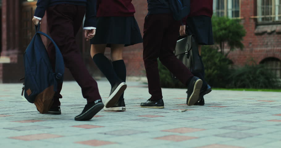 Back view on the feet of the schoolchildren in the uniforms and with bags walkingthe school yard before or after classes.