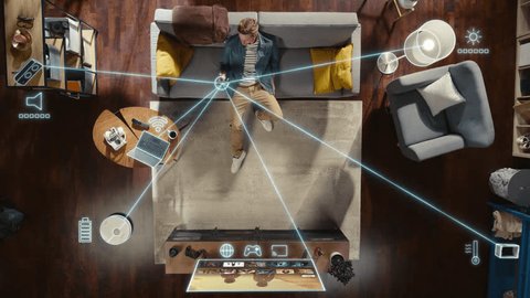Top View Of Caucasian Man In the Loft Apartment Sitting Down on The Couch and Connecting Smartphone to Convenient Smart Home System. VFX Animation Visualizing Connected Devices. Laptop, TV, Speaker., videoclip de stoc