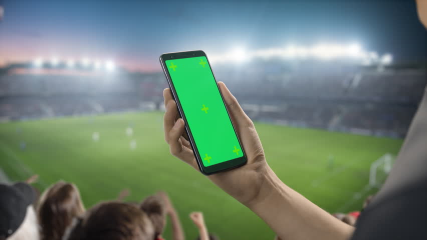 Sport Stadium Championship: Person's Hand Holding Green-Screen Chroma Key Smartphone. Sports Match with Fans on Tribune Cheering for Favourite Team to Win. Isolated POV Close-up Copyspace Template. Royalty-Free Stock Footage #1100838929