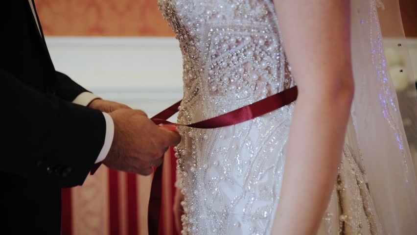 An unknown man as usual someone from close family ties a red ribbon around the bride's waist. Concept of Turkish wedding tradition | Shutterstock HD Video #1100845447