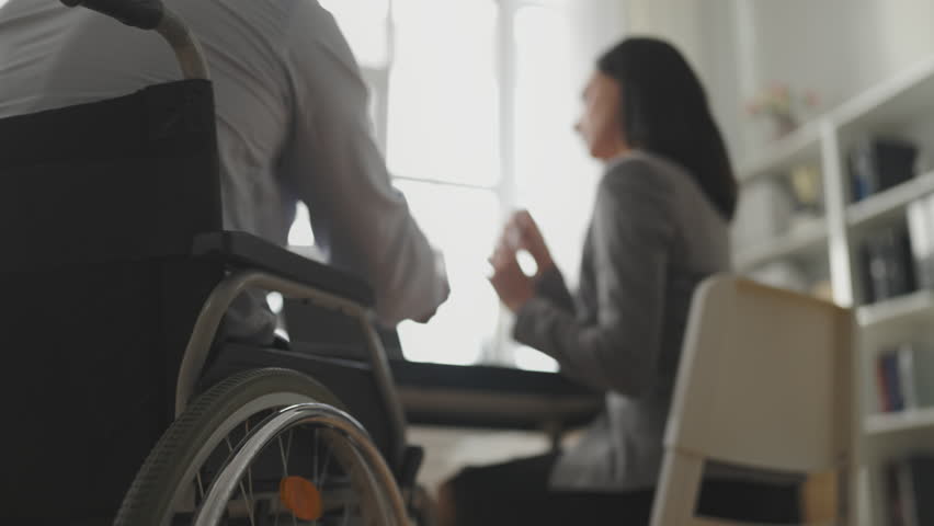 Closeup of man wheelchair user sharing ideas with female colleague in office | Shutterstock HD Video #1100845457