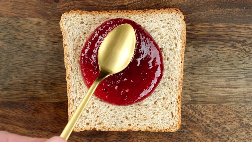 Raspberry jam spreading on bread with a golden spoon, top view. Perfect traditional breakfast Royalty-Free Stock Footage #1100845521