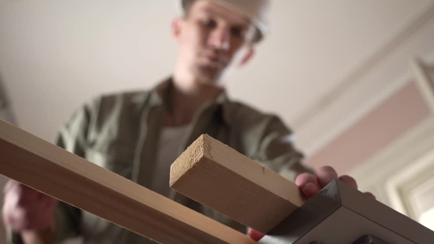 young male carpenter sawing a plank on the workbench. Home activity.