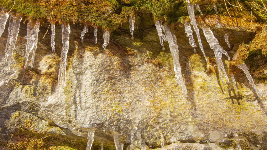 Icicles on the side of a sandstone cliff melt, drip and refreeze as shadows indicate the movement of the sun - time lapse