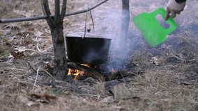 A man blows a fire with food being cooked on it in a cauldron with a plastic spatula. Slow motion video.