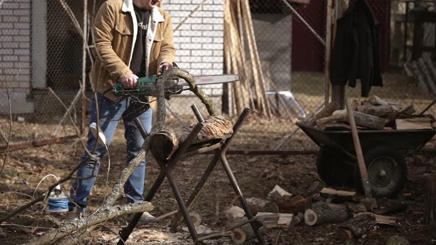 Young man sawing branches on a sawhorse with a chainsaw