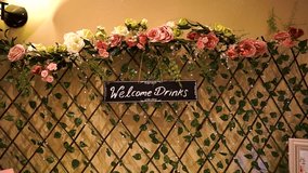 Welcome drinks sign hanging on a multicolour decorated wooden fence with ace shape and flowers around for a wedding