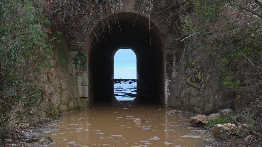 A tunnel leads towards a wild sea, where incoming waves create a rippling effect