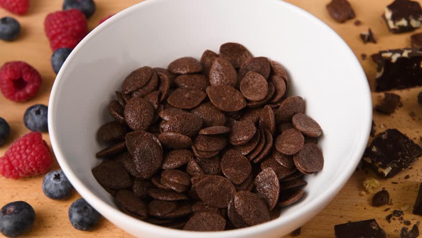 Shot of milk being poured into a bowl of chocolate cereal.