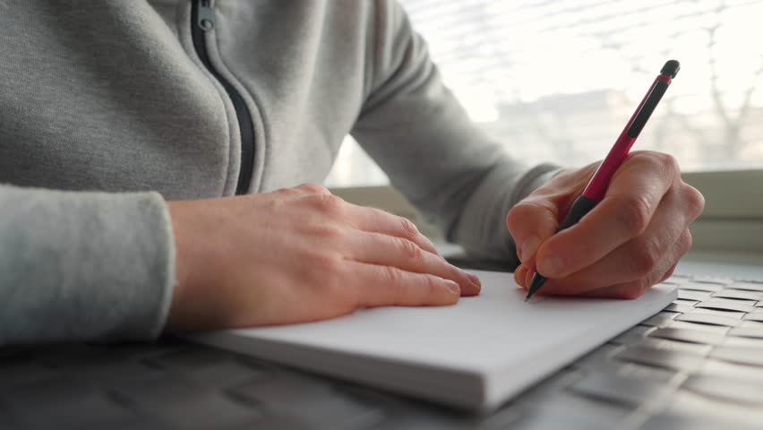 Left-handed man writing on paper next to a window Royalty-Free Stock Footage #1100858347