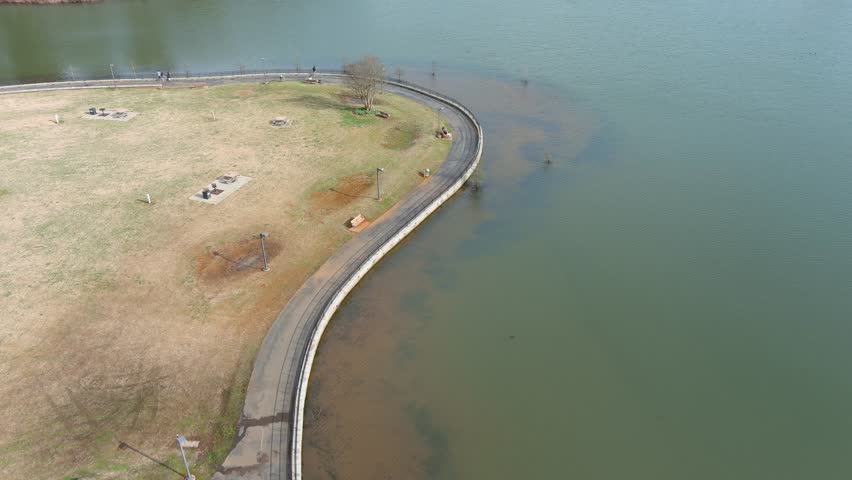 descending aerial footage of gorgeous winter landscape at Lawrenceville Lake with people walking, lush green trees, yellow grass, blue sky and clouds at Rhodes Jordan Park in Lawrenceville Georgia USA