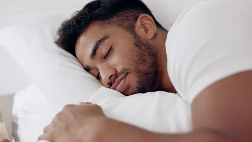 Face of happy man sleeping in bed, morning and at home for relaxing wellness, comfortable pillow and healthy rest. Young guy asleep in bedroom with smile, happiness and peaceful dreams on mattress Royalty-Free Stock Footage #1100864991