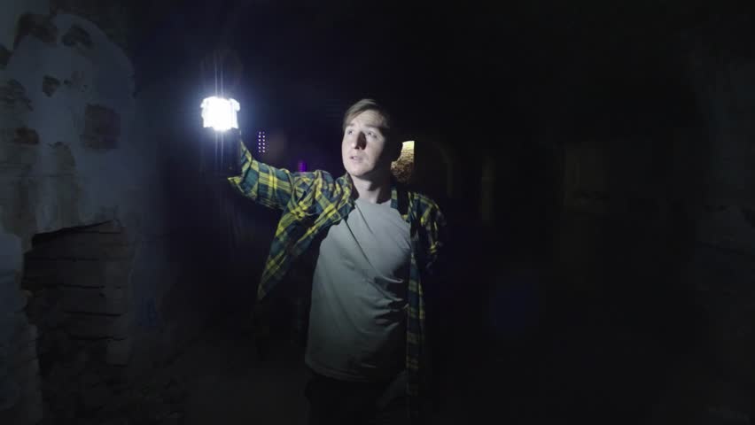 A man with a lantern in the dungeon. The man goes a dark tunnel and holds a pantry. Concept: research, expedition, mysticism, mystery, unknown. High quality 4k footage