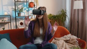 Portrait of woman using virtual reality futuristic technology VR app headset helmet to play simulation 3D 360 video game, watching film movie at modern home apartment. Girl in goggles sitting on couch