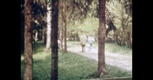 People couple walk in pine summer forest. Beautiful spruce green park. Man, woman in nature background. 1980s. Vintage archival color film. Fir trees, clean environment. Retro archive. Old archives
