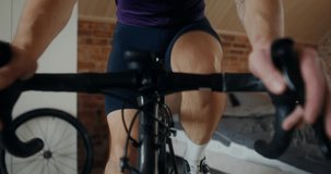Young sporty man cycling in modern home interior using bicycle holding station, dynamic indoor video