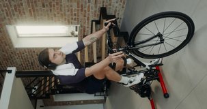 Athletic build man in sportswear and headphones uses bike simulator for cardio training at home, indoor vertical video in stylish modern interior