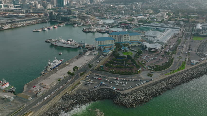 Buildings and harbour on sea coast. Tilt up reveal of cityscape and high mountains. Cape Town, South Africa