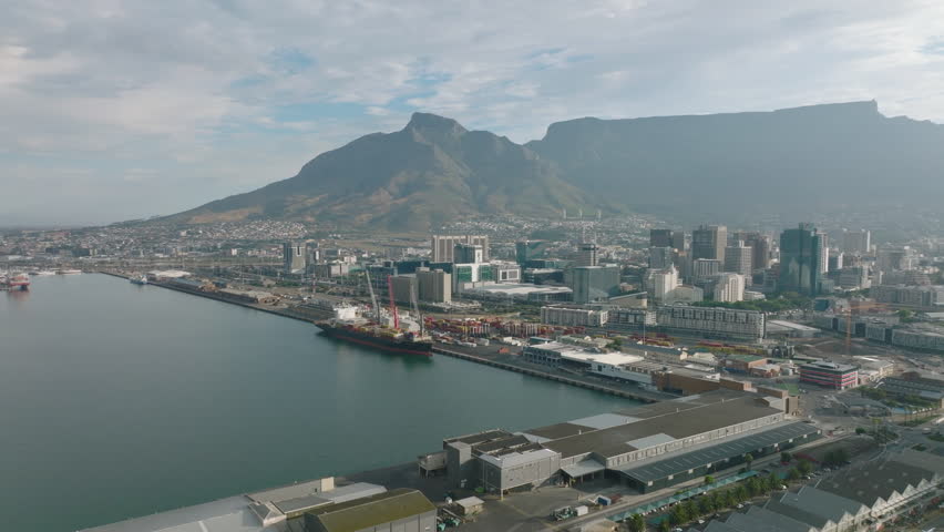 Coastal borough with harbour. Industrial and logistic sites in city. Flat mountain ridge in background. Cape Town, South Africa